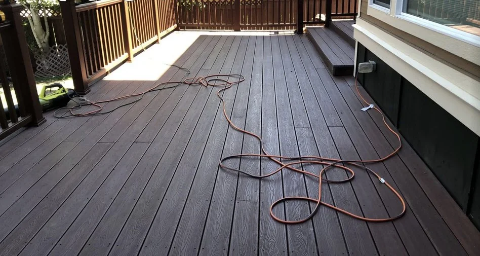 Dark brown composite deck with a railing and stairs down to the yard, an extension cord still lying on the boards